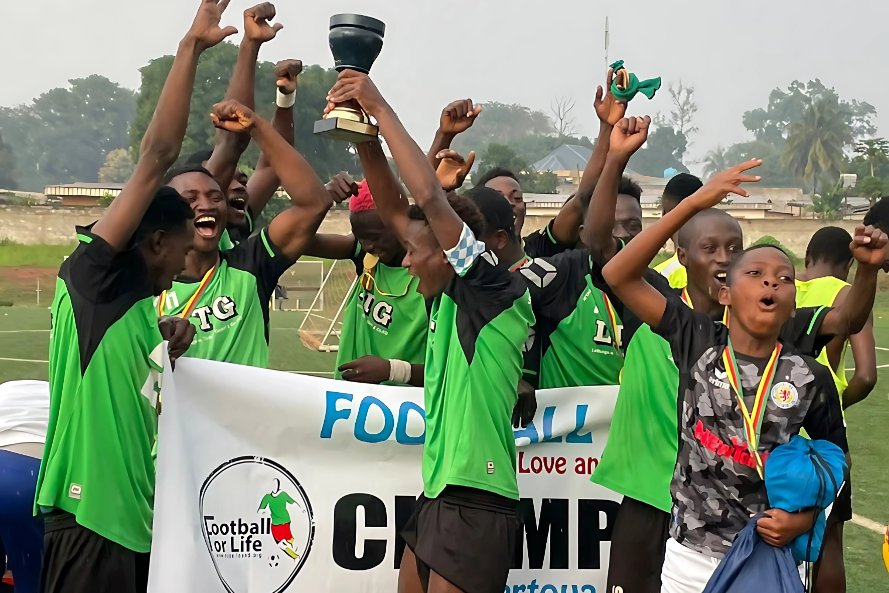 Etwa zehn Jugendliche des Projektes Forrestcup jubeln in grünen Fußballtrikots auf einem Fußballfeld in Ost-Kamerun. Sie halten einen Pokal in die Höhe.