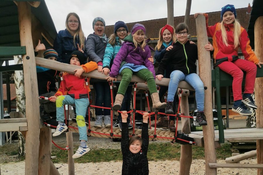Zehn Mädchen und Jungen im Grundschulalter sitzen oder hängen auf einem Klettergerüst und lächeln in die Kamera.